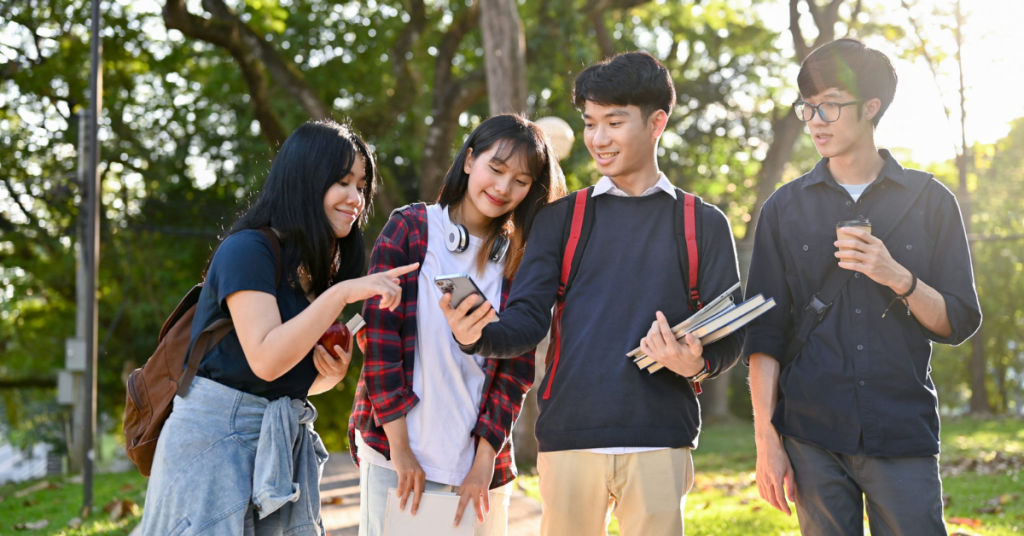 A group of smiling young Asian college students talking and walking in the campus park together.