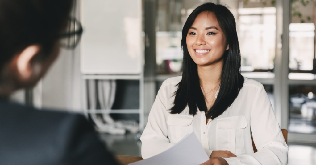 Portrait of smiling person smiling and holding resume while sitting in front of interviewer during meeting