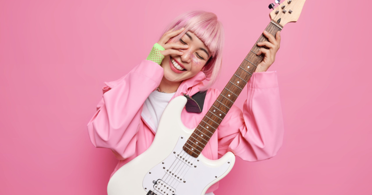 Person wearing all pink, in front of a pink backdrop, holding guitar