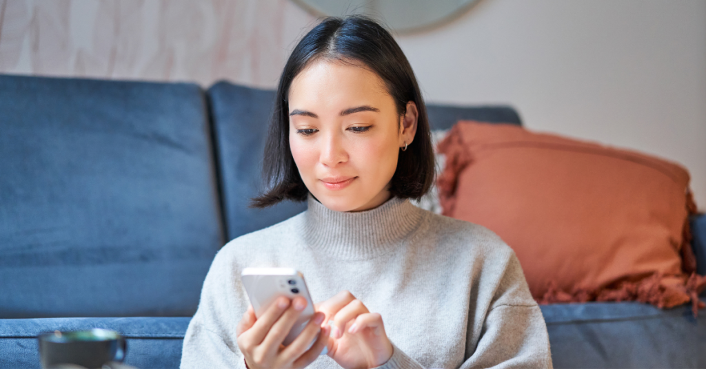 portrait-smiling-asian-woman-sits-home-uses-smartphone-app-orders-delivery-messages-someone