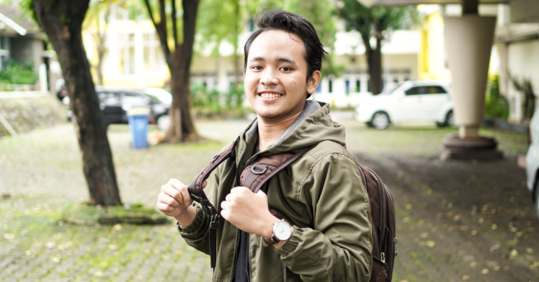 Person outside and smiling into camera, holding backpack