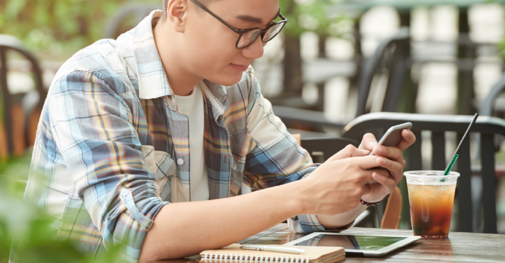 young-asian-male-student-sitting-street-cafe-using-smartphonehappiness while using smartphone communication home background technology ideas concept