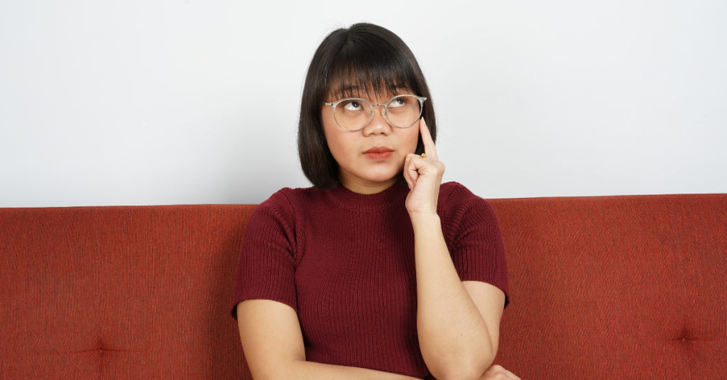 woman wearing red shirt sitting on couch looking up thinking