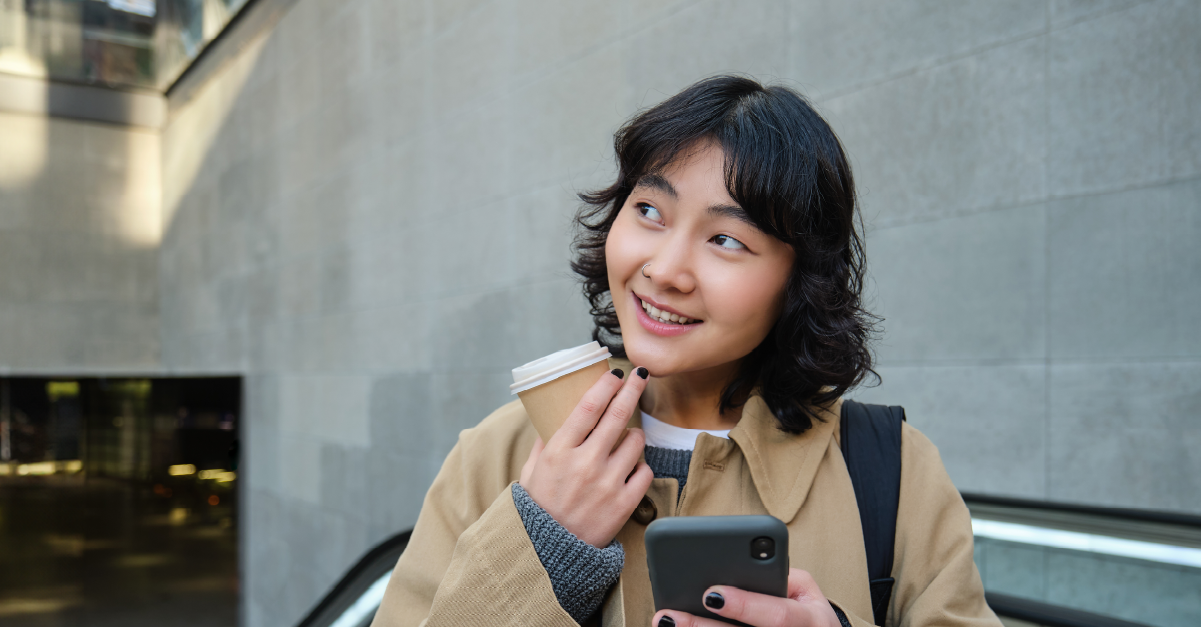 beautiful-happy-asian-girl-drinks-coffee-go-using-mobile-phone-while-standing-escalator