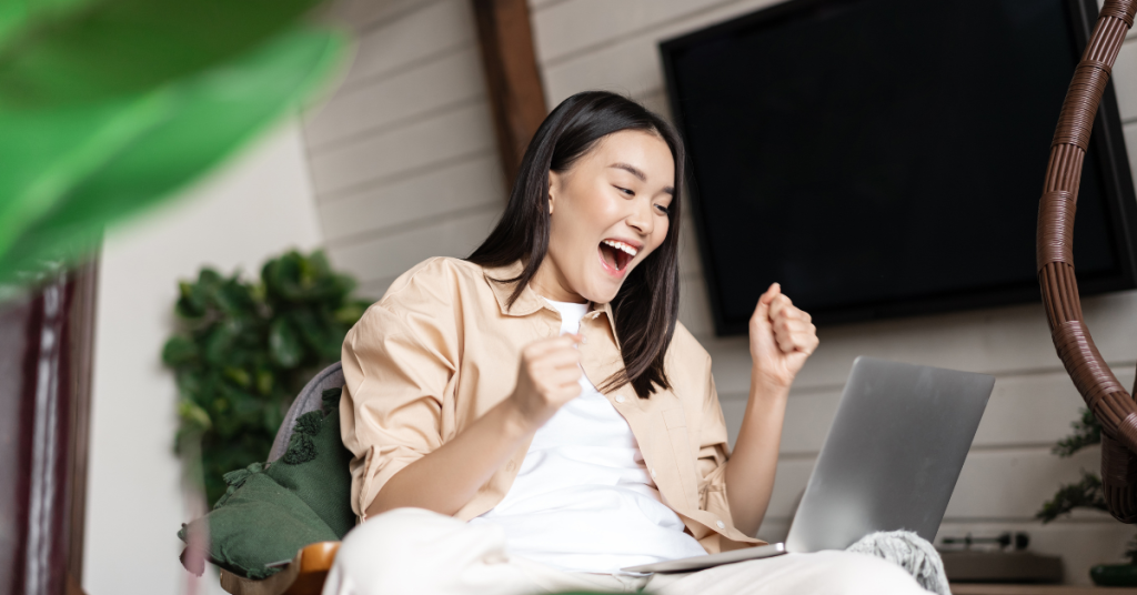 excited-asian-girl-rejoicing-after-looking-laptop-screen-sitting-home-cheering