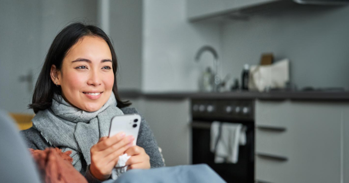 Closeup of a woman on the couch with a scarf, holding her smartphone in two hands, after Sending Money to the Philippines