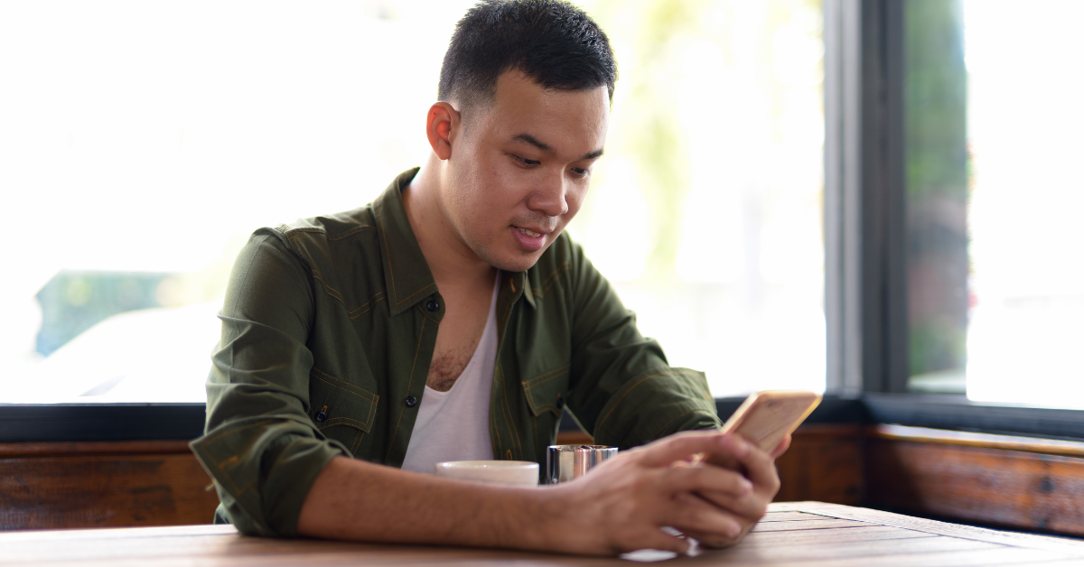 person in a coffee shop, sitting down and looking at their smartphone