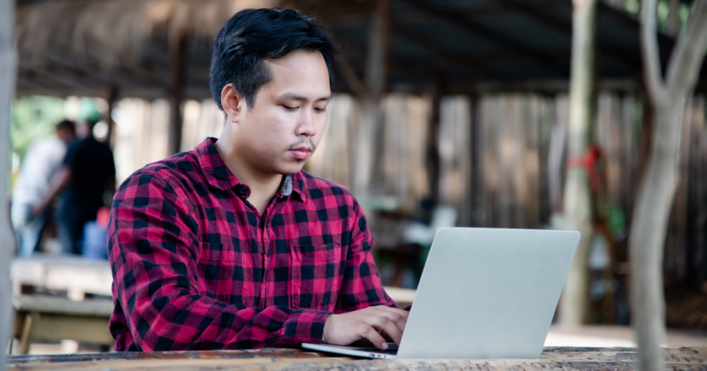 young man sitting with his laptop on a table outside