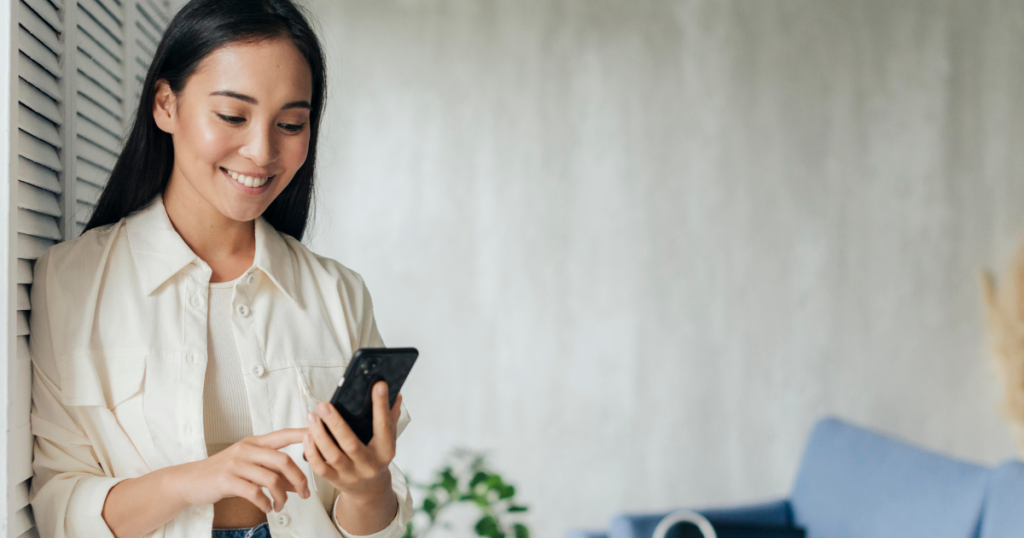smiling woman leaning against wall, looking at phone