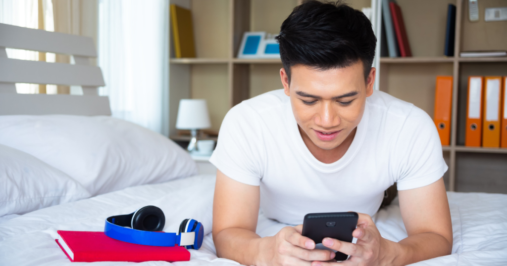 send remittance: Man laying on his bed at home, on his phone