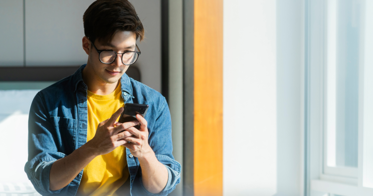 Young man on his phone, wearing a yellow shit and denim button down