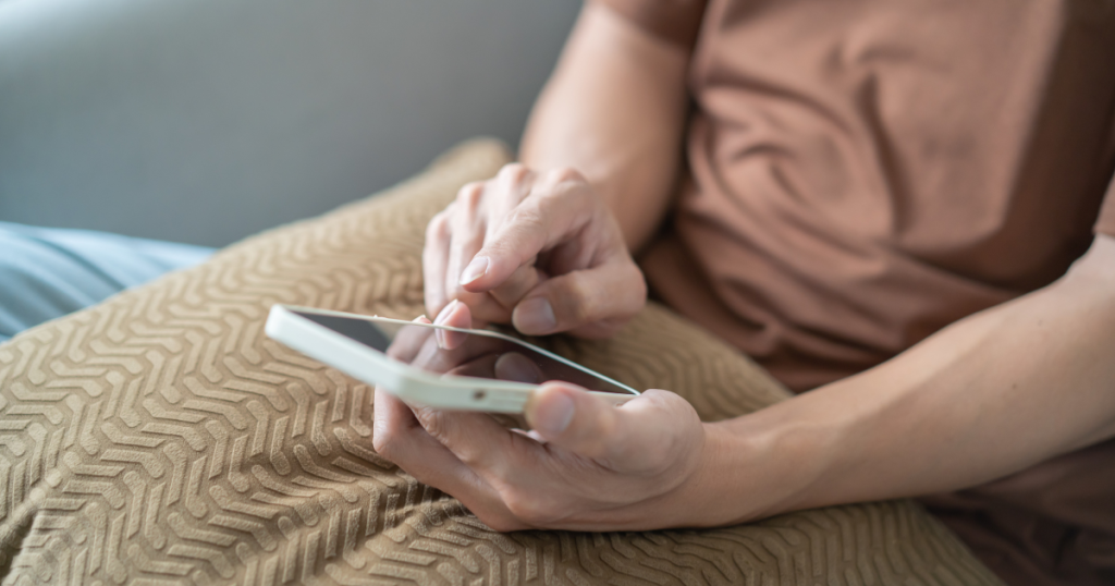 Closeup of someone sitting down with a pillow on their lap, scrolling on their phone