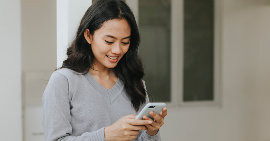 Woman standing and smiling while scrolling on her smartphone