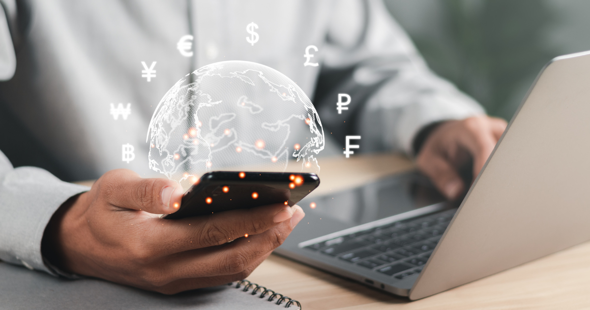 Closeup of someone on their laptop and smartphone with animations of a globe and currencies coming out of the phone
