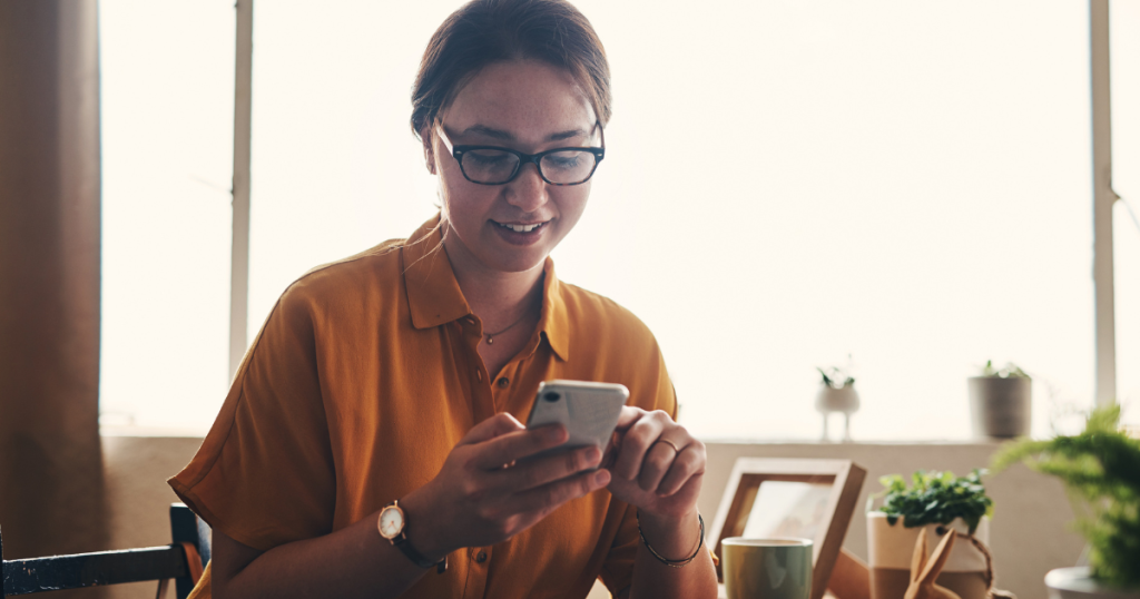 woman in orange blouse sitting down and scrolling through her smartphone