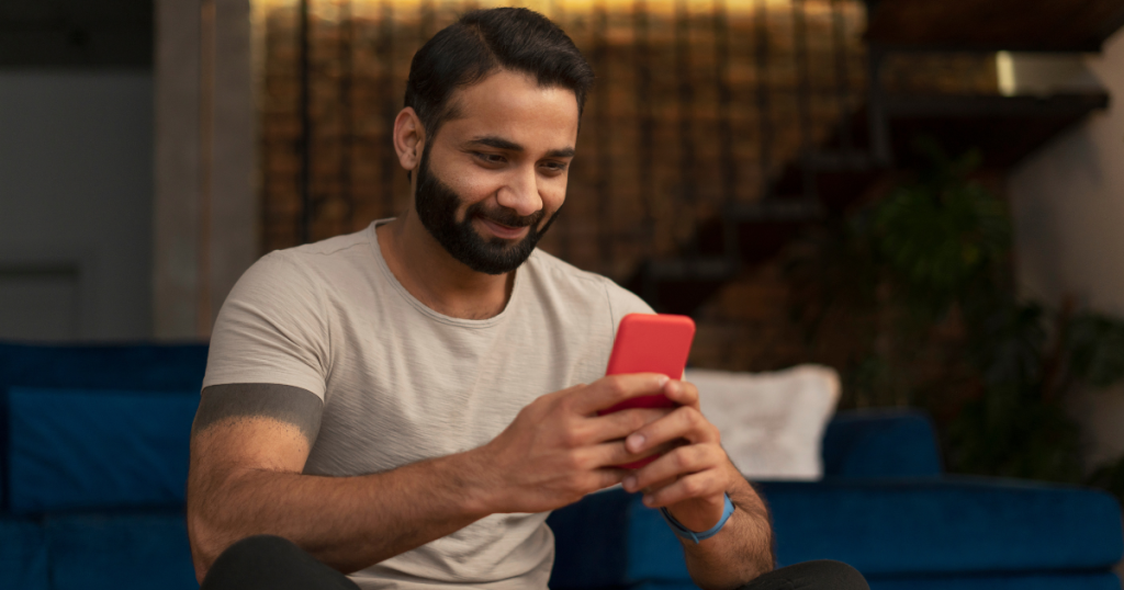 Young man smiling, sitting down, smiling looking at phone