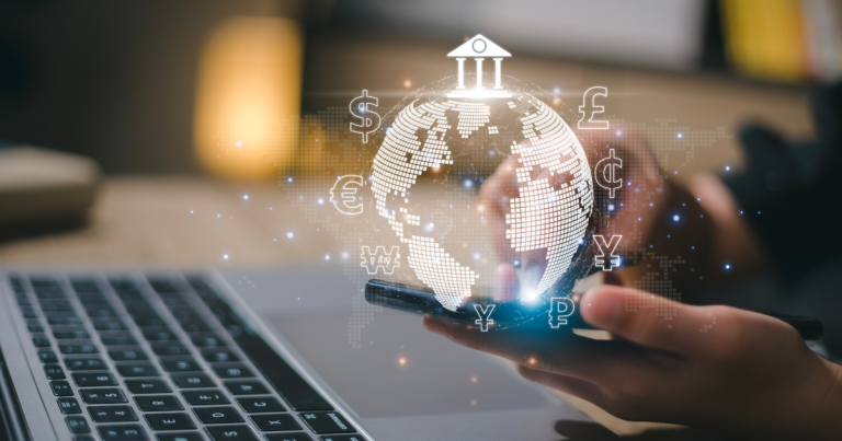 What does remit mean: closeup of someone sitting in front of their laptop, while holding their smartphone with an animation of a globe and currencies come out of the screen