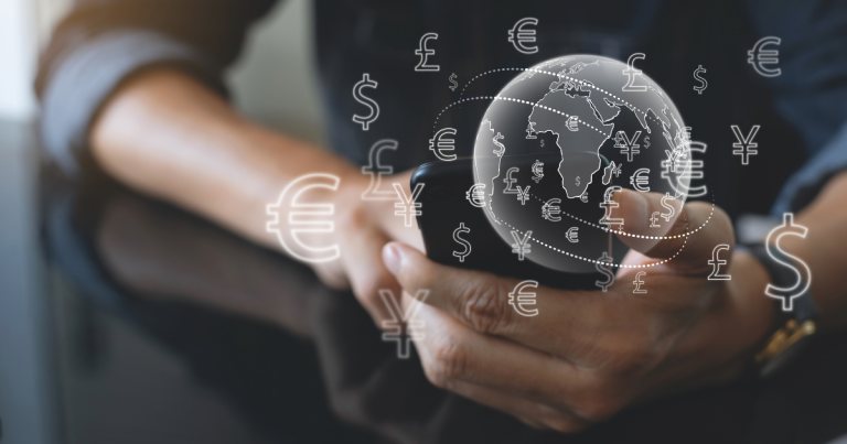 Close up of a person seated at a desk holding their smartphone, with an animation of a globe and currencies coming out of the phone