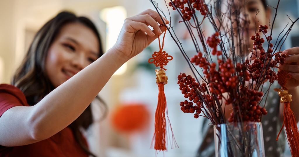 Closeup of woman hanging a red decoration on plant for Lunar New Year